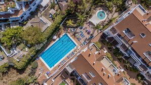 An aerial view of a resort with a central swimming pool, multiple lounge areas, and surrounding greenery.