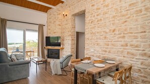 A cozy living room with a stone wall, a fireplace, a flat-screen TV, and a dining area with wooden furniture.