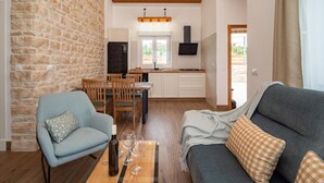 A cozy living room with a sofa, a dining table with chairs, a kitchen area, and a stone wall.