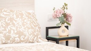 A bed with a patterned pillow, a vase with flowers, and a small table with a light-colored vase.