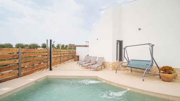 A swimming pool with a wooden fence, lounge chairs, and a swing chair.