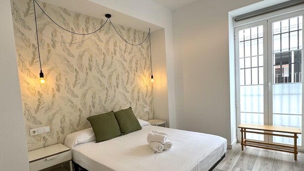 A bedroom with a bed, nightstands, a bench, and a window with blinds.