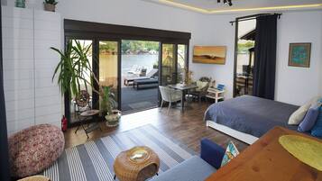 A modern bedroom with a large bed, a desk, and a view of a body of water through a sliding glass door.