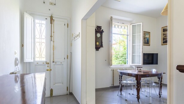 A room with a wooden table, chairs, a clock, and a window with an open door.