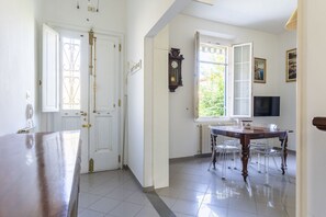 Una habitación con una mesa de madera, sillas, un reloj y una ventana con puerta abierta.