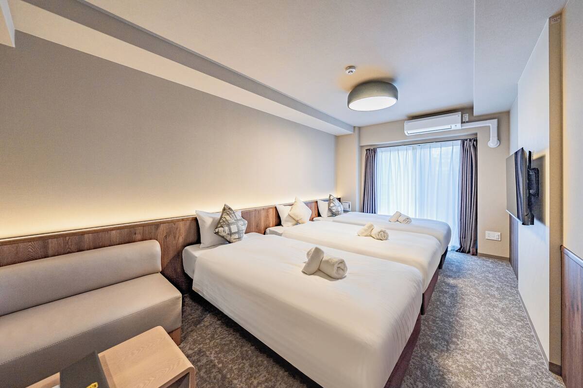 Une chambre d’hôtel avec deux lits, un canapé, une télévision et une fenêtre avec des rideaux.