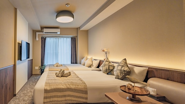 A hotel room with a large bed, a sofa, a TV, and an air conditioning unit. - Apartment Hotel 11 Tsutenkaku (Osaka)