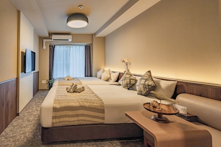 A hotel room with a large bed, a sofa, a TV, and an air conditioning unit.