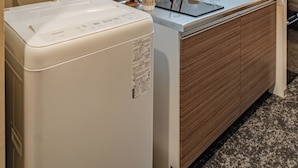 A compact kitchen with a built-in oven, a sink, and a microwave. There is a small shelf with decorative items and a potted plant. - Apartment Hotel 11 Tsutenkaku (Osaka)