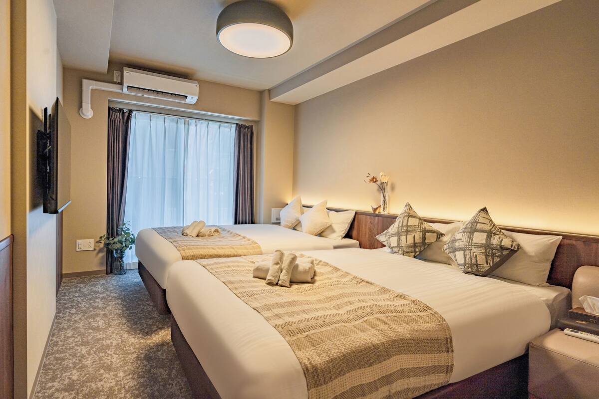 Une chambre d’hôtel avec deux lits, un téléviseur à écran plat, un appareil de climatisation et une fenêtre avec des rideaux.
