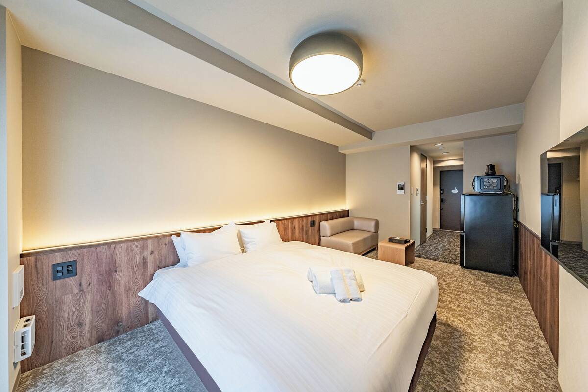 Une chambre d’hôtel avec un grand lit, une tête de lit en bois, un petit coin salon et une kitchenette.