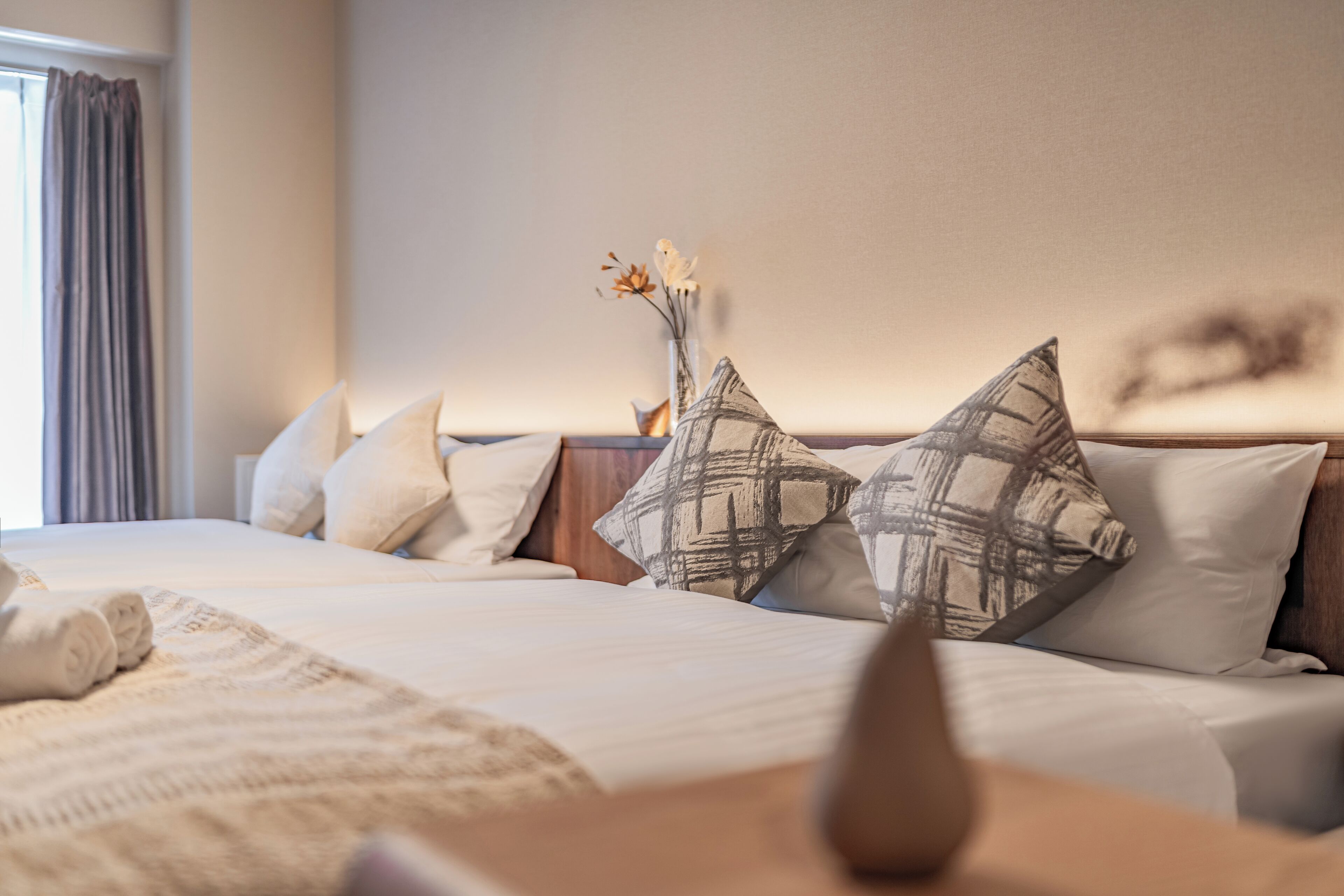 A neatly made bed with white linens and a decorative vase with flowers on the nightstand.