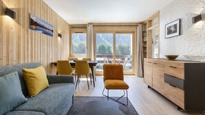 Una sala de estar moderna con un sofá, sillas, una mesa de comedor y una cocina con armarios de madera y un ventanal grande.