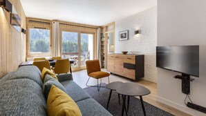 Una sala moderna con sofá, mesa de comedor, sillas, televisor y zona de cocina con un mueble y ventana.