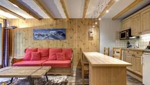 A cozy room with a wooden interior, a red sofa, a wooden dining table, and a kitchen area with wooden cabinets and a microwave.
