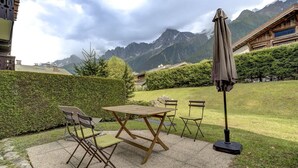 An outdoor seating area with a table and chairs, a standing umbrella, and a view of mountains in the background.