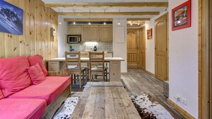 A cozy interior with a wooden ceiling, a kitchen area with wooden cabinets, a dining table, and a pink sofa.