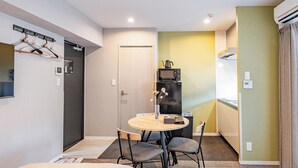 A compact hotel room with a round table, two chairs, a small refrigerator, a microwave, and a TV. - Apartment Hotel 11 Umeda Kamiyama (Osaka)