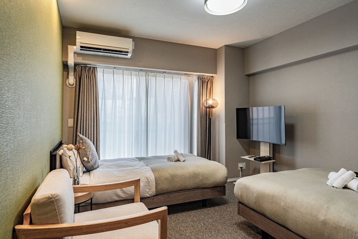 Quarto de hotel com duas camas, uma televisão, um aparelho de ar condicionado e um abajur.