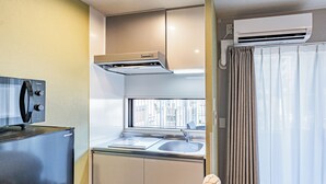 A compact kitchenette with a microwave, stove, and sink. - Apartment Hotel 11 Umeda Kamiyama (Osaka)