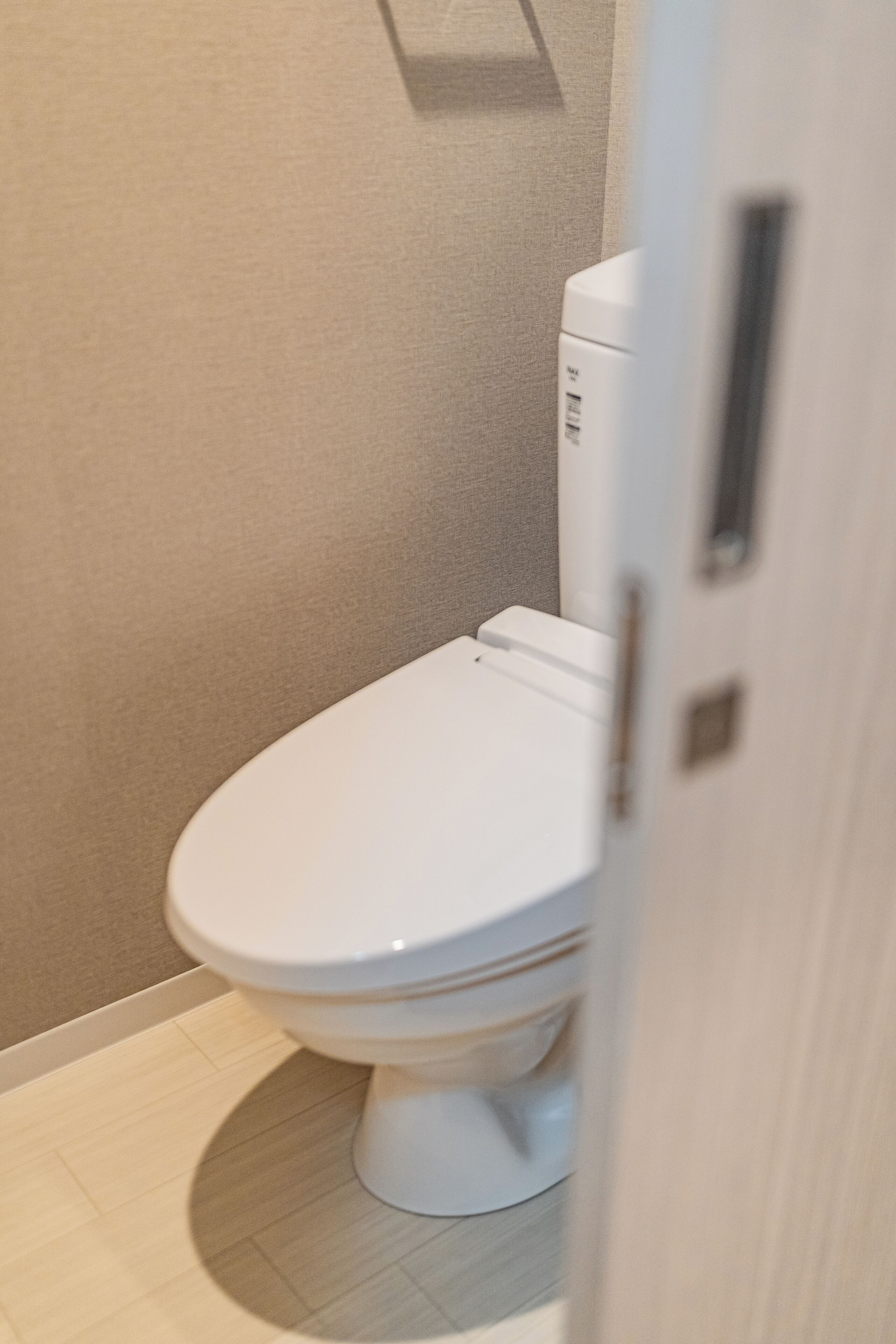 A white toilet in a bathroom with a beige wall and light-colored floor tiles.
