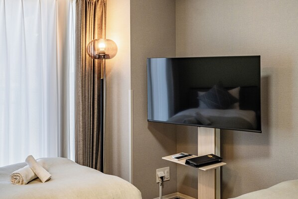 Habitación de hotel con cama, televisor de pantalla plana montado en la pared, mesita de noche con control remoto y lámpara.