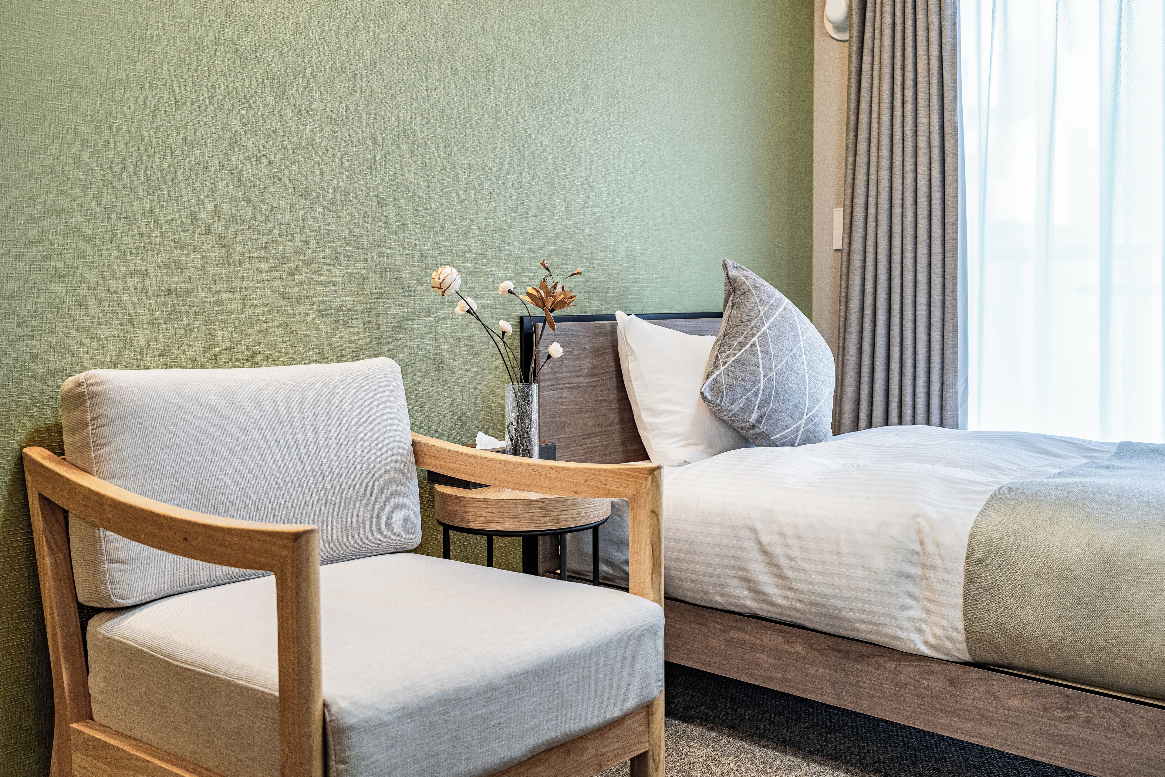 Une chambre d’hôtel avec un lit, deux chaises, une petite table et un vase avec des fleurs.