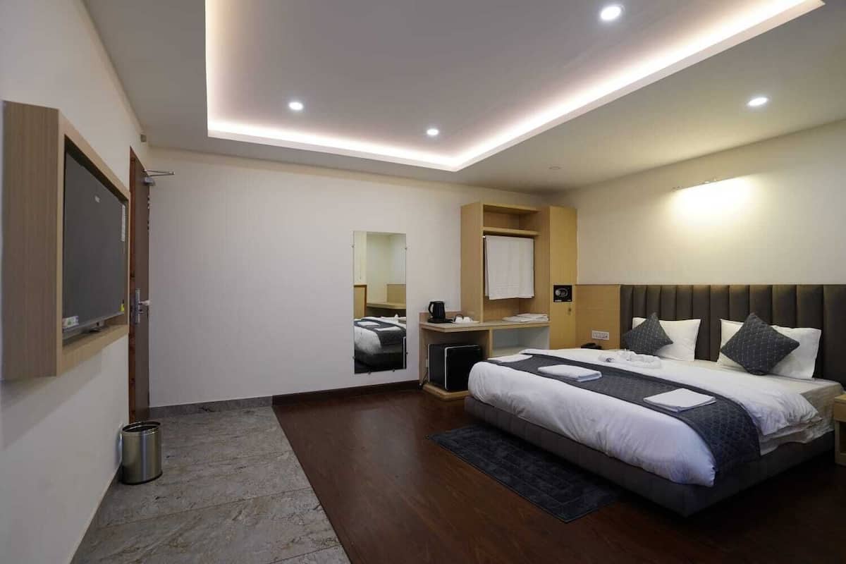 A modern hotel room with a large bed, a desk, a mirror, and a small bathroom area.