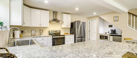 A modern kitchen with white cabinets, a granite countertop, stainless steel appliances, and a small dining area with a wooden table.