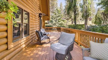 Une terrasse en bois, meublée de mobilier en osier, avec vue sur les arbres.