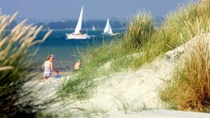 A beach scene with sand dunes and a clear view of sailboats on the water. - Two Bed Seafront Escape in East Wittering (East Wittering)
