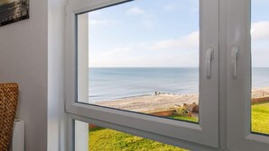 A room with a large window overlooking a beach. - Two Bed Seafront Escape in East Wittering (East Wittering)