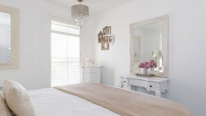 A bedroom with a bed, a dresser, a mirror, and a chandelier. - Two Bed Seafront Escape in East Wittering (East Wittering)
