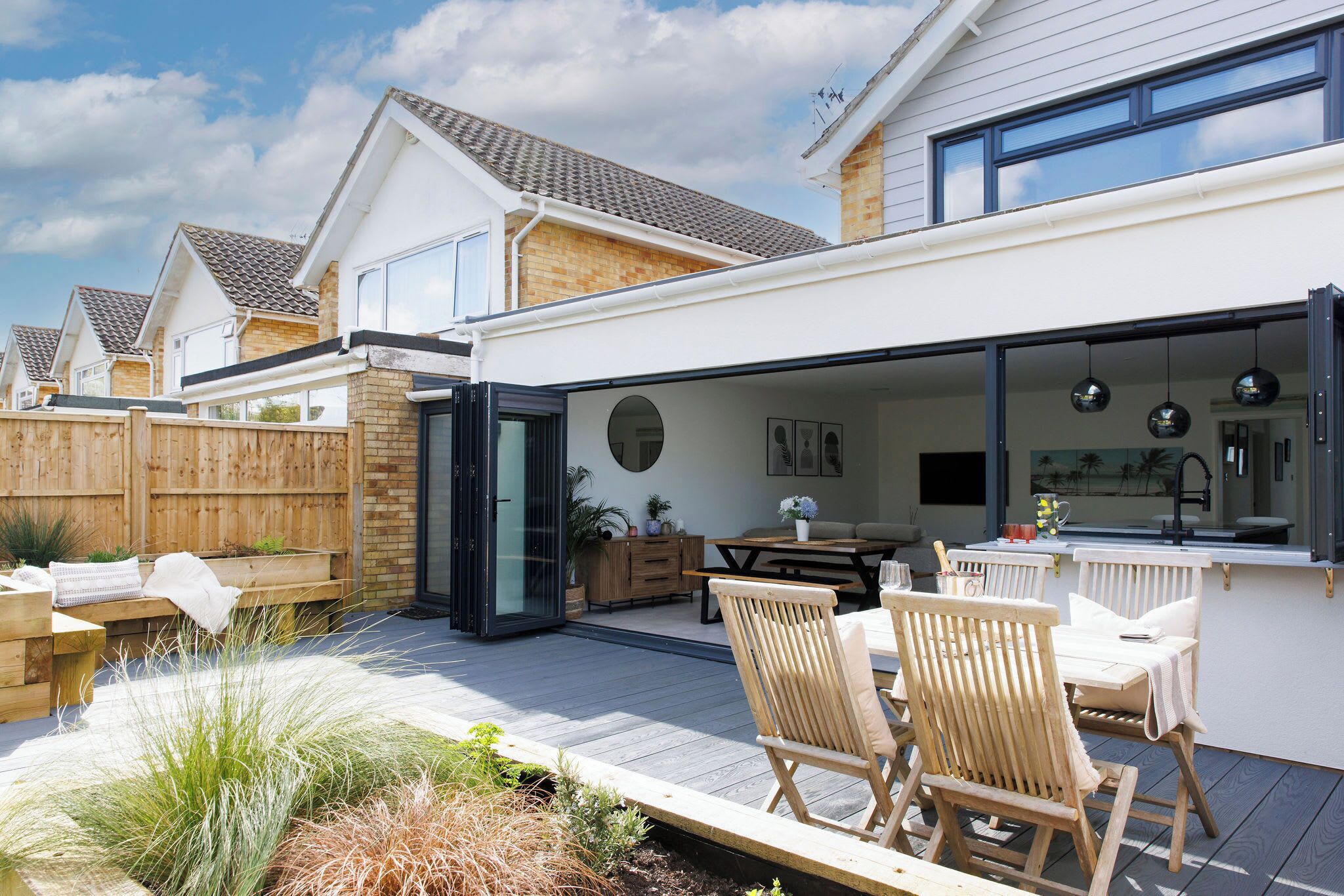 A modern outdoor patio with wooden furniture, a dining table, and a kitchen area with a sink and counter.