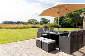 An outdoor patio with a dining table, chairs, and a large umbrella. - Charming 3-Bed Country Cottage with Hot Tub (West Wittering)