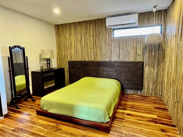 Un dormitorio con una cama, una mesita de noche, un espejo, una lámpara y una ventana.
