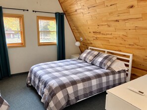 A bedroom with a bed, a nightstand, a lamp, and a window with curtains.
