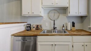 Una cocina con armarios blancos, un lavavajillas de acero inoxidable, una encimera de madera y un reloj en la pared.