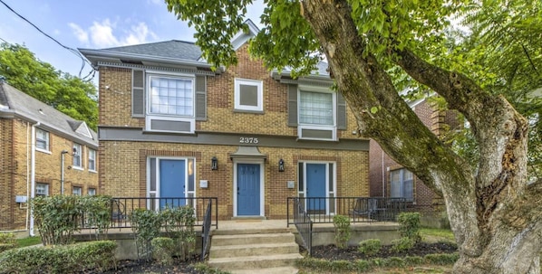 A two-story brick house with a blue door, numbered 2375, and a tree in the foreground. - Your Home Away from Home (Memphis)