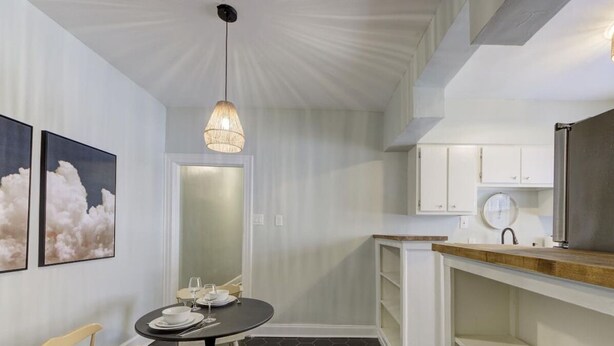Cocina compacta con armarios blancos, encimera de madera y una lámpara colgante.