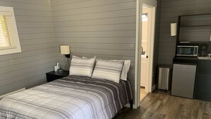 Una camera da letto con un letto, un comodino, una lampada e vista sull'area della cucina.