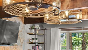 Een moderne woonkamer met een open haard, een televisie en een groot raam met uitzicht op bomen.