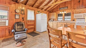 Une cuisine chaleureuse, aménagée dans le style d’un chalet, avec des murs en bois, une table à manger, des chaises, un réfrigérateur et une horloge au mur.