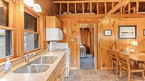 L’intérieur d’un chalet en bois comprend un coin cuisine équipé d’un évier, d’un four à micro-ondes et d’une table à manger avec des chaises.