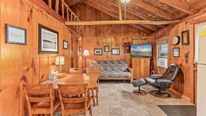 L’intérieur d’une cabane comprend une table à manger en bois, des chaises, un canapé, un téléviseur et une cheminée.