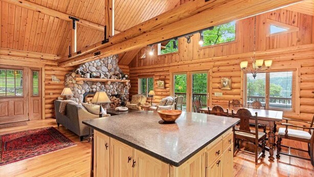 A log cabin interior with a stone fireplace, wooden furniture, and a large island in the center. - Black Squirrel Retreat (Minong)