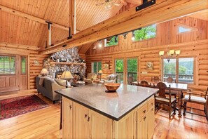 A log cabin interior with a stone fireplace, wooden furniture, and a large island in the center. - Black Squirrel Retreat (Minong)