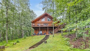 A wooden cabin with a balcony, surrounded by trees. - Black Squirrel Retreat (Minong)