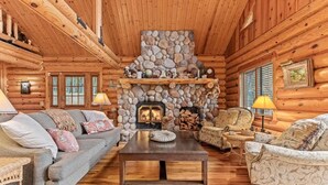 A log cabin interior with a stone fireplace, wooden furniture, and a cozy seating area. - Black Squirrel Retreat (Minong)