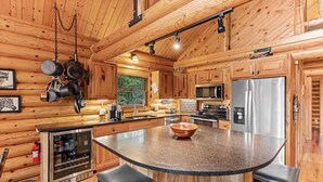 A wooden cabin interior with a kitchen featuring a granite island, stainless steel appliances, and a refrigerator. - Black Squirrel Retreat (Minong)
